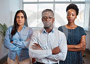 Group of serious business people pose arms folded in office, diverse trio