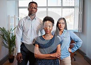 Group of serious business people pose arms folded in office, diverse trio