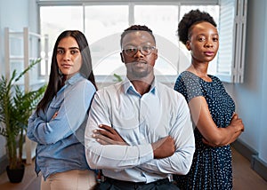 Group of serious business people pose arms folded in office, diverse trio