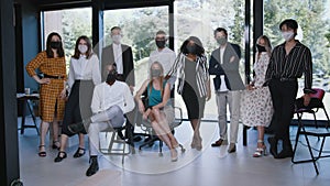 Group of serious young multiethnic business people posing looking at camera wearing COVID-19 masks at modern office.