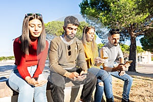 Group of serious young people sitting on a city wall spending time using smartphone with mobile connection. New normal human