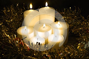 Group of seven burning candles on a black background and with green and red garland.