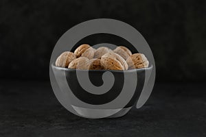 a group of shell walnuts in a black texture bowl on a black background