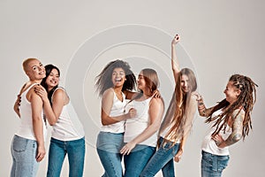 Group of six beautiful diverse young women wearing white shirt and denim jeans having fun, laughing while posing