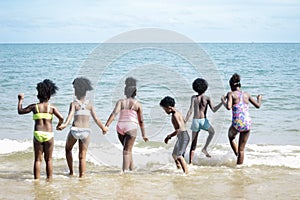 Group of six boys and girls standing in a line in shallow sea water, cute kids having fun on sandy summer beach, happy childhood