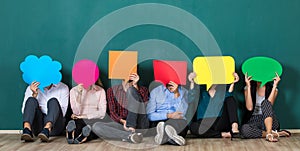 Group of six business people team sittiing together and holding colorful and different shapes of speech bubbles over their faces