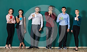 Group of six businesspeople colleague in modern company standing together in a row in front of the green wall and holding coffee