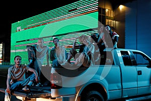 A group of six good-looking casually dressed youngsters of different nationalities sitting in an opened pick-ups trunk