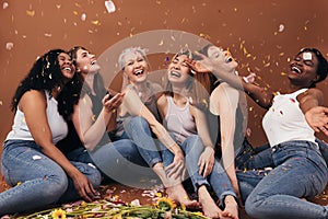 Group of six laughing women of different ages sitting under falling flower petals. Multi-ethnic smiling females having fun in photo