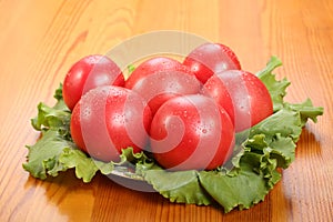 Group of six red ripe tomatoes with water drops lie on a lettuce leaves on a table