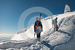 group of skiers in bright ski suits with backpacks and ski equipment on snowy ridge.