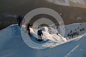 group of skiers in bright ski suits are walking at snow-covered mountain trail