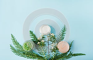 Group of small cosmetic jars with cream and salt for bath on blue background with greenery with a copy space