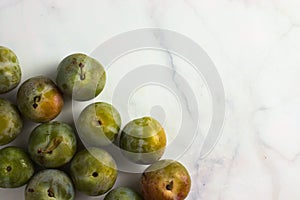 Group of small greengage plums on white marble, top view, copy space