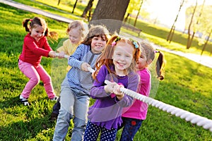 A group of small preschool children play a tug of war in the park.