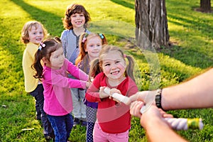 A group of small preschool children play a tug of war in the park.