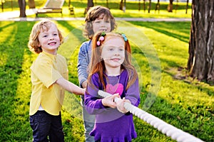 A group of small preschool children play a tug of war in the park.