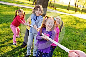 A group of small preschool children play a tug of war in the park.