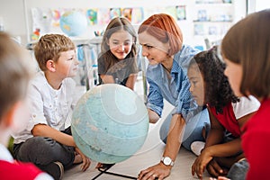 A group of small school kids with teacher sitting on the floor in class, learning.