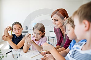 A group of small school kids with teacher sitting on the floor in class, learning.