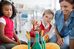 A group of small school kids with teacher sitting on the floor in class, learning.