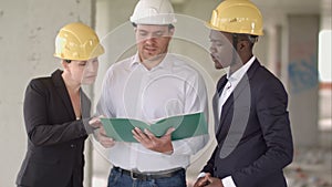 Group of smiling builders in hardhats with clipboard and blueprint outdoors