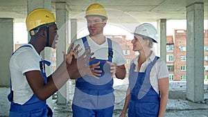 Group of smiling builders in hardhats talking at construction site