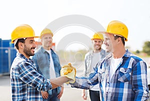 Group of smiling builders shaking hands outdoors