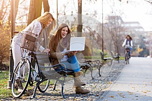 Group of smiling college girls on park bench working on laptop