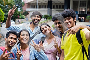 Group of smiling college students taking selfie by holding camera at college campus - concept of friendship, education