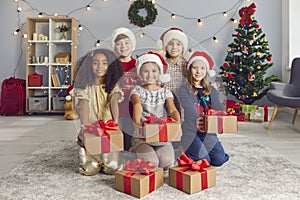 Group of smiling diverse children holding out Christmas gift boxes tied with red ribbons