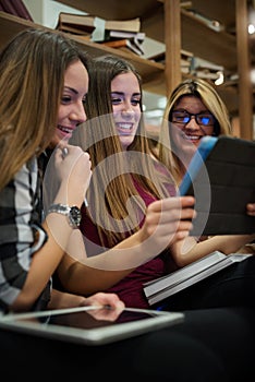 Group of smiling female students looking at tablet in library