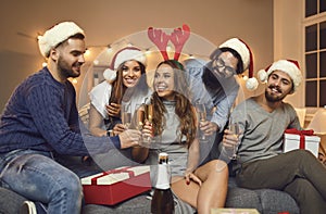 Group of smiling friends in holiday caps and accessories feasting Christmas with champagne