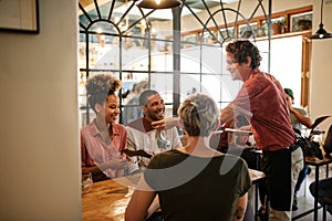 Group of smiling friends ordering food from a bistro waiter