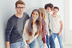 A group of smiling friends is standing in a bright room with a window.