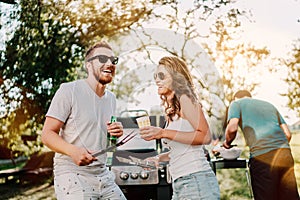 Group of smiling friends in vacation having beers and cooking on garden barbecue. Lifestyle, leisure concept