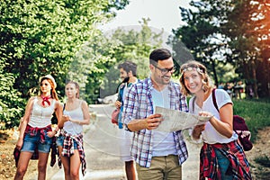 Smiling friends walking with backpacks in woods - adventure, travel, tourism, hike and people concept