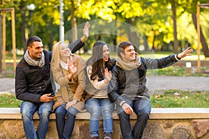 Group of smiling friends waving hands in city park