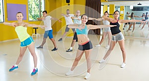 Group of smiling men and women exercising in studio