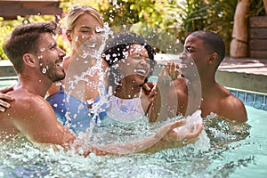 Group Of Smiling Multi-Cultural Friends On Holiday Splashing In Swimming Pool 