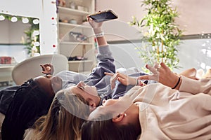 Group Of Smiling Multi-Cultural Teenage Girl Friends Posing For Selfie On Mobile Phone At Home