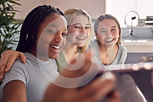 Group Of Smiling Multi-Cultural Teenage Girl Friends Posing For Selfie On Mobile Phone At Home