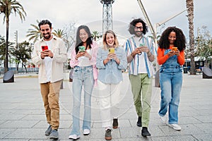 Group of smiling multiracial young people using their mobile phones, walking on the street, laughing and having fun