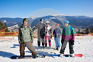 Group of smiling people on skis and snowboard in deep snow on background of winter mountains.