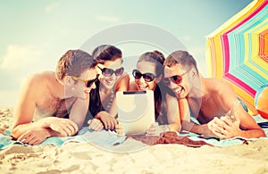 Group of smiling people with tablet pc on beach