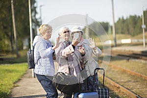 Group of smiling senior women take a self-portrait on a platform waiting for  train to travel during a COVID-19 pandemic