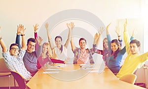 Group of smiling students raising hands in office