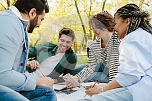 Group of smiling students using smartphone while spending time together in park