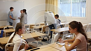 Group of smiling teen pupils chatting in break between lessons indoors