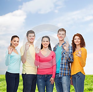 Group of smiling teenagers over blue sky and grass